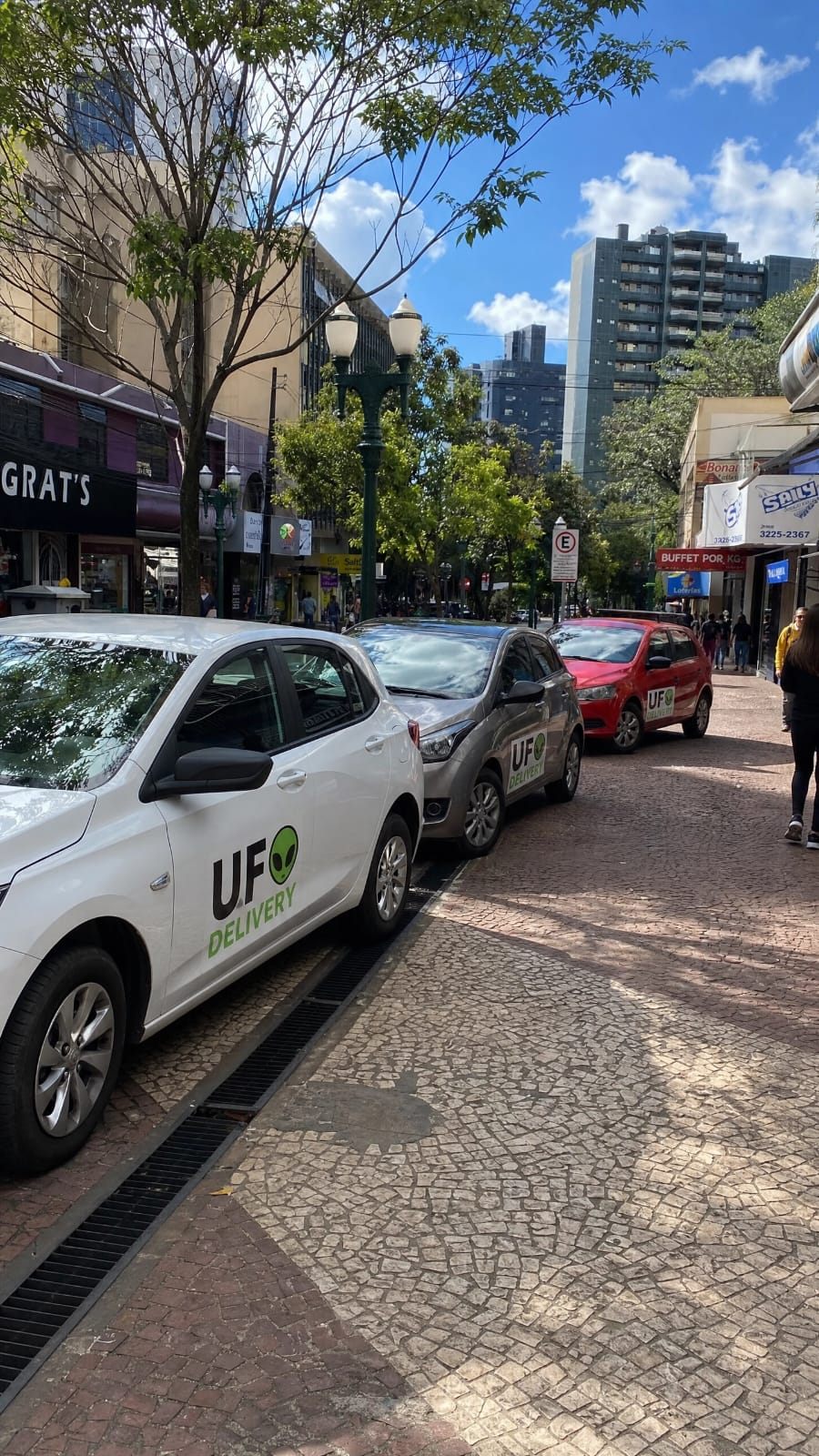 Três carros da frota UFO Delivery estacionados em rua de comércio